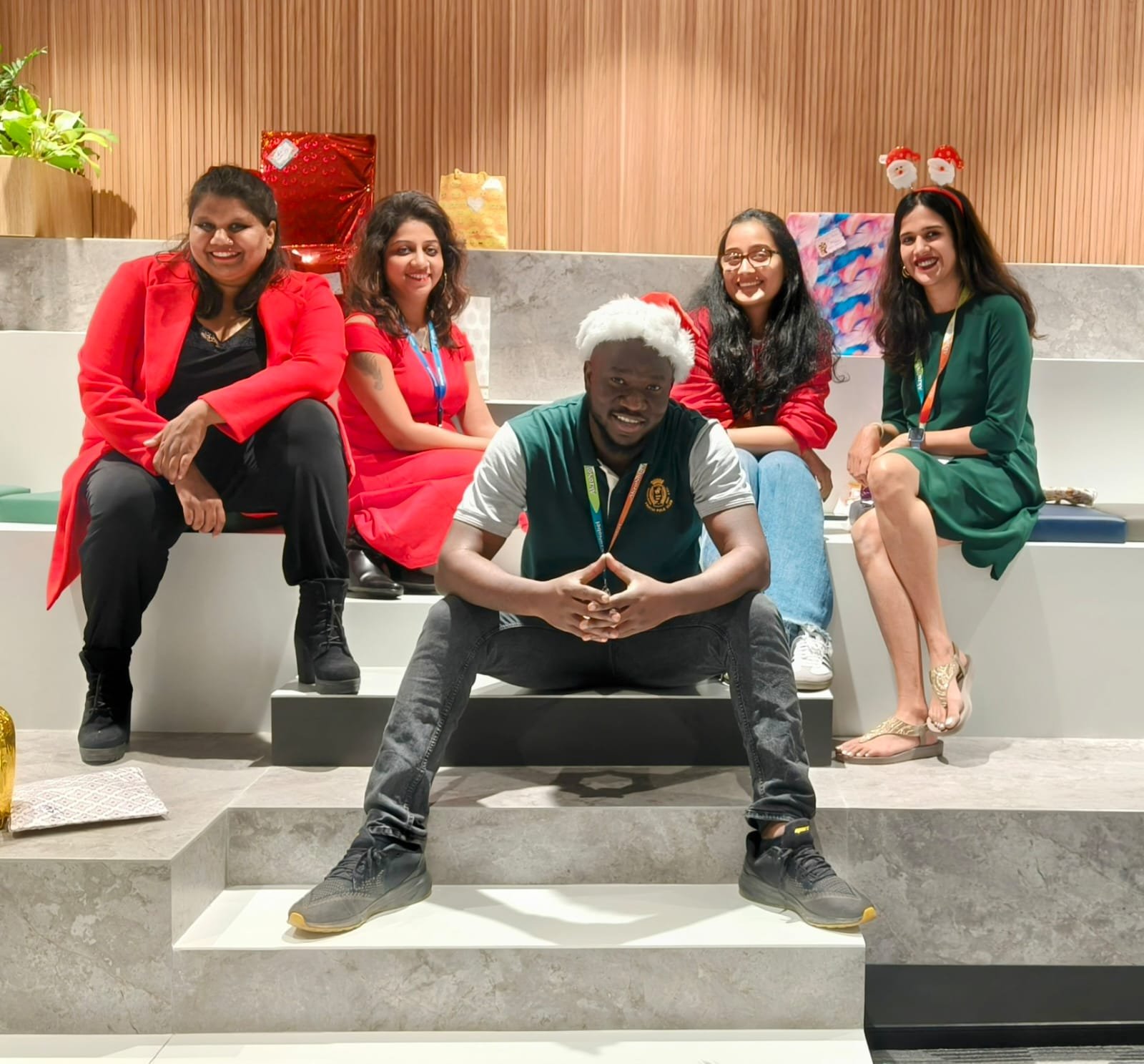 Jean Michel in a Santa hat sitting on steps with four colleagues dressed in red and green for Christmas